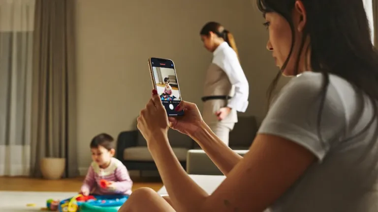 mãe verificando câmera de babá pelo celular enquanto criança brinca sozinha em casa
